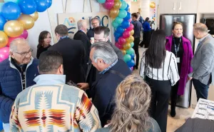 Group of people gathered chatting near logo wall with baloons at new AIOC Enoch office opening